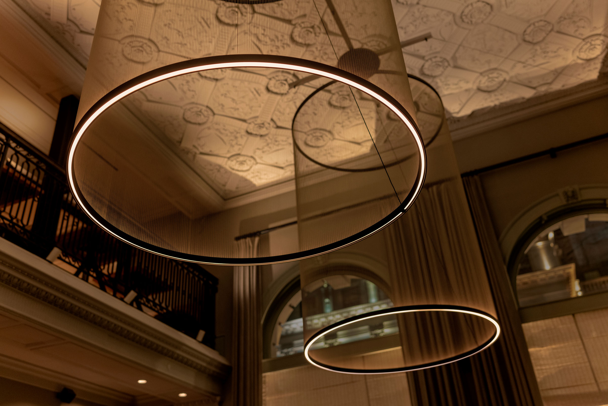 Sculptural ring luminaires beneath an ornate ceiling