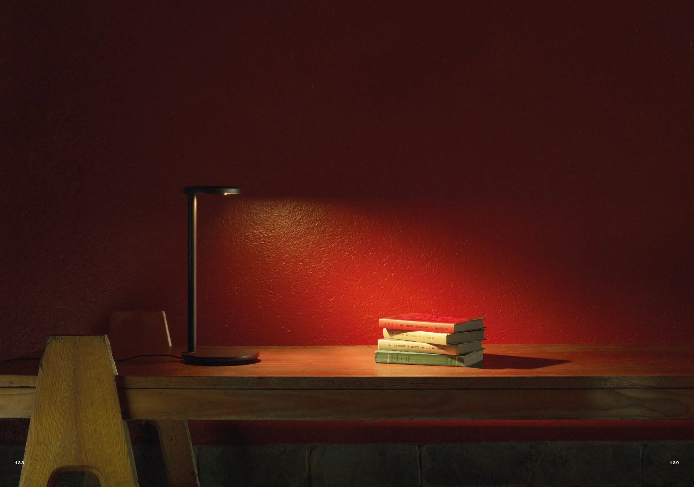 Reading lamp and a stack of lighting catalogues on a red wall backdrop