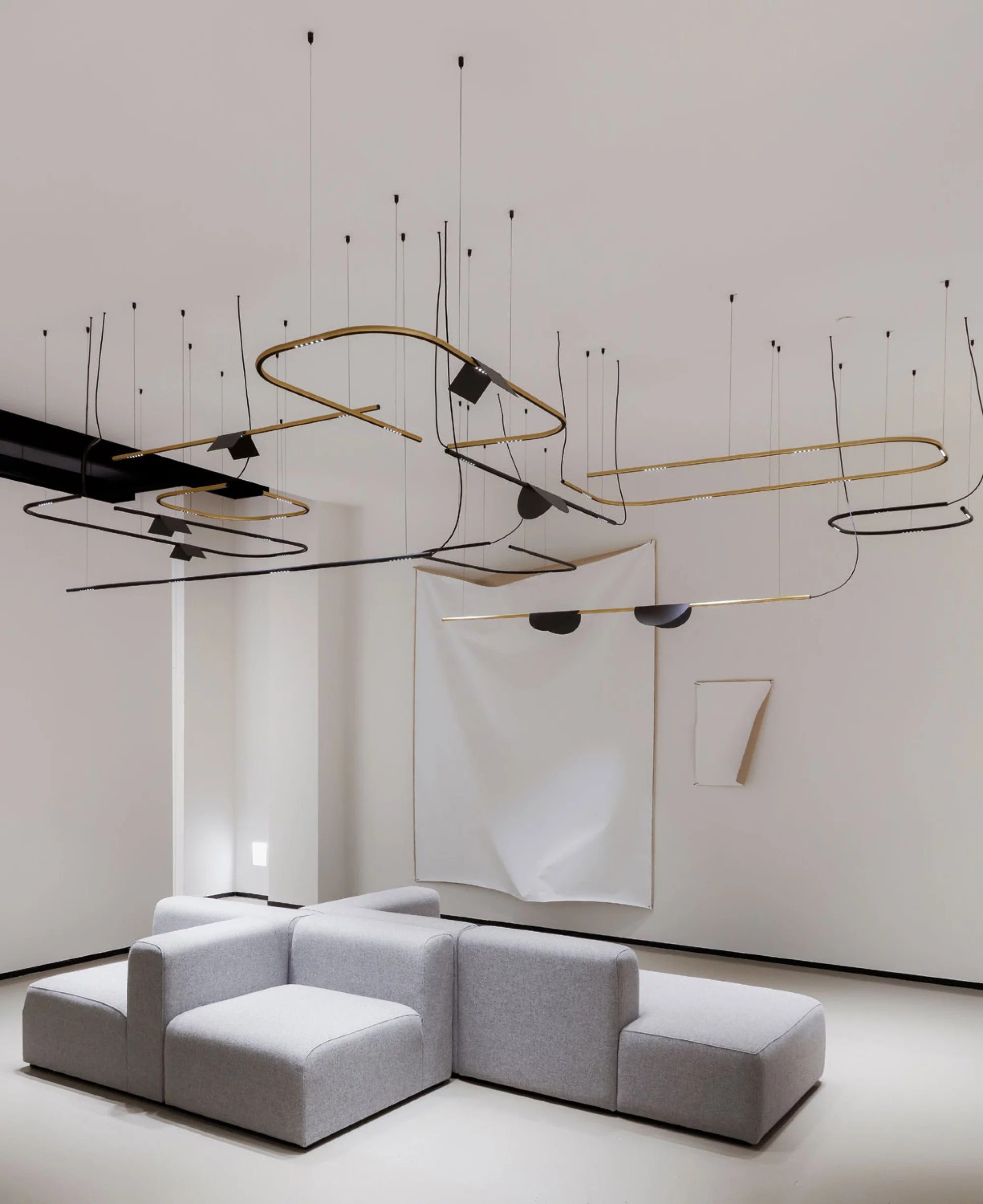 Gallery space with freeform brass and black linear luminaires above modular seating
